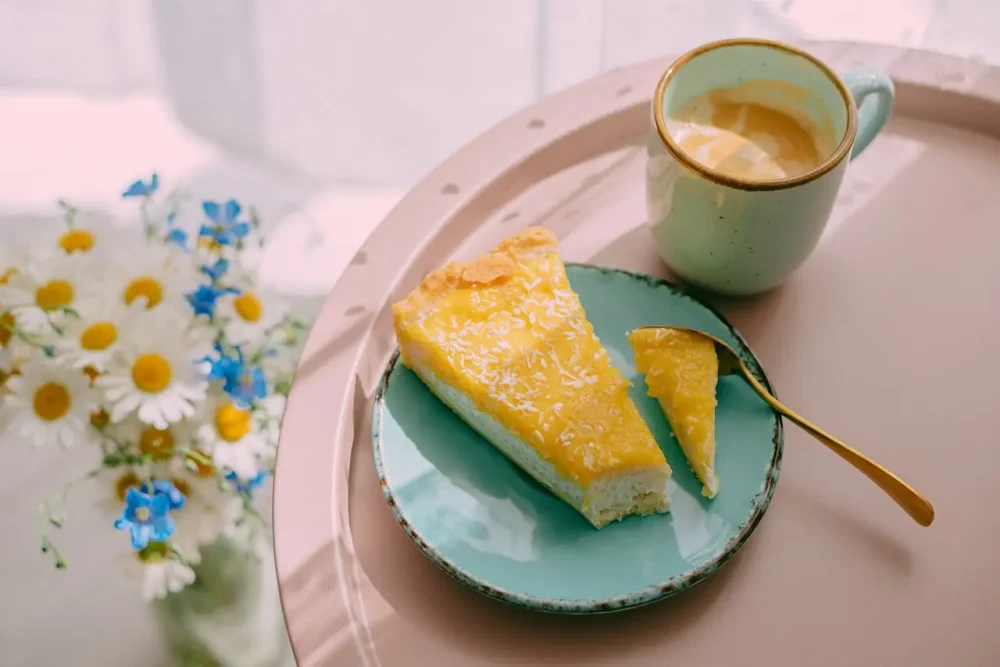 a slice of floral tart and a cup of coffee on a table, with some garden flowers next to them